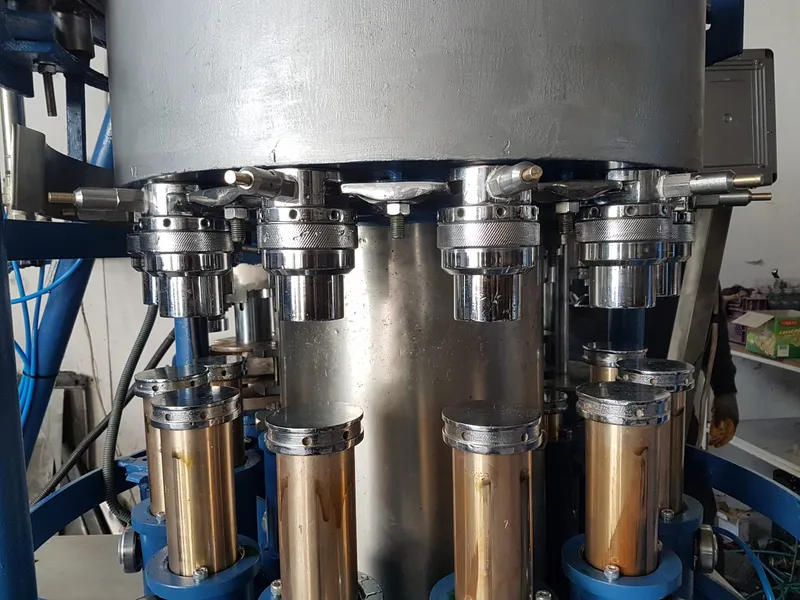 Atölyede rotary dolum ve kapaklama makinesinin paslanmaz dolum başlıkları, yakından